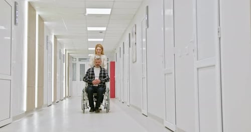 Nurse Assisting Elderly Man in Wheelchair Through Hospital Hallway