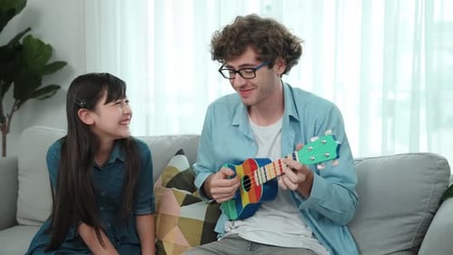 Man plays ukulele with smiling girl on couch