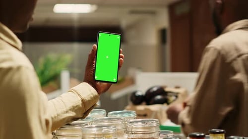 African American Storekeeper Holding Phone with Greenscreen in Grocery Store