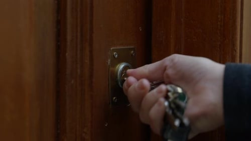Close up on hand turning key locking old wooden brass door keyhole lock