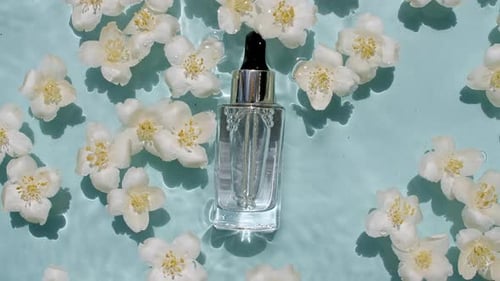 Kosmetikflasche, Fläschchen und Jasminblüten auf der Wasseroberfläche, mit Tropfen