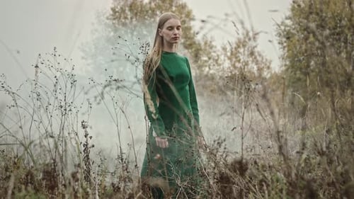 Blonde woman wearing green dress standing in a field posing for fashion photoshoot