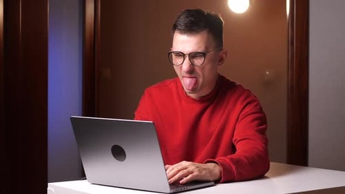 Ein junger Mann arbeitet an einem Laptop und zeigt seiner Zunge das Konzept eines Internetkommentators