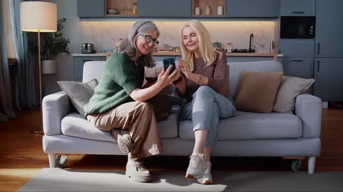 Two Senior Women Relaxing at Home with Smartphone