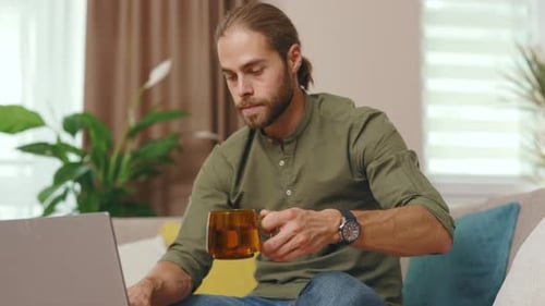 Man Using Laptop and Drinking Beverage on Sofa