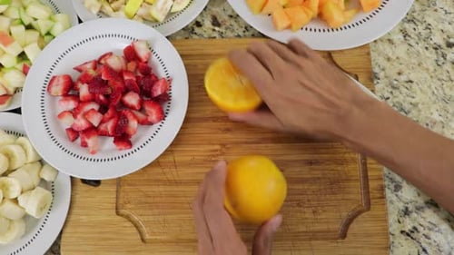 Top view of male hands cutting oranges into equal halves on cutting board. No face.