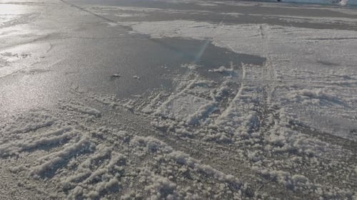 Pull back over snow covered blacktop parking lot on a sunny day.