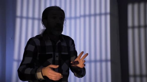 Man Gesturing in Dark Room with Barred Window