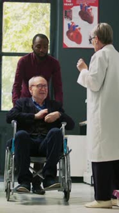 Doctor Consults Senior Patient in Wheelchair with Caregiver