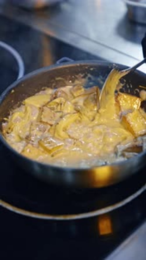 Preparing the potatoes in the cheese sauce. Cook stirs the dish in frying pan. Close up.