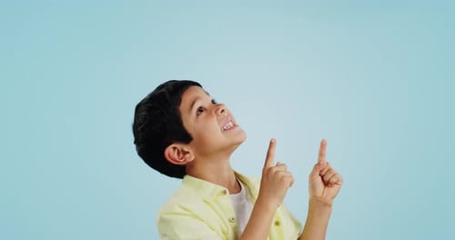 Kid, boy and smile while pointing in studio on blue background with mockup for announcement