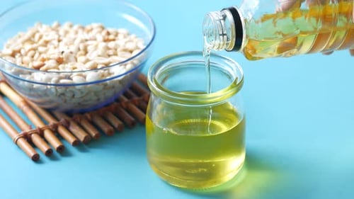 Derramando óleo de amendoim em jarra de vidro