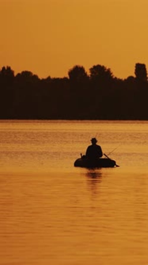 Boot mit einem Fischer im Sonnenuntergangslicht schwebt langsam auf dem See.