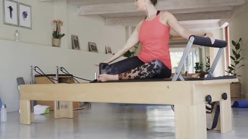Fit senior caucasian woman stretching on reformer in pilates studio, unaltered, in slow motion