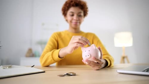 Ein schönes afroamerikanisches Mädchen stapelt Münzen in einem Sparschwein