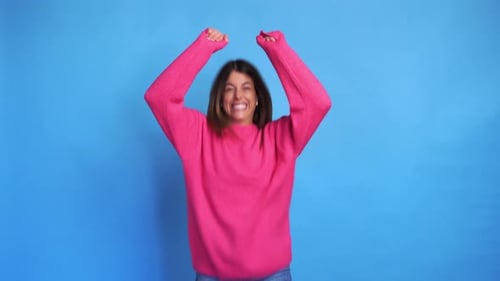 Woman Celebrates with Arms Raised Against Blue Background
