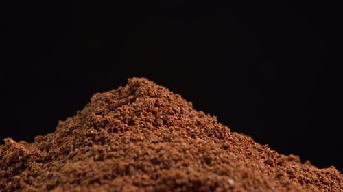 Café molido natural que gira en cuenco de madera sobre fondo negro. Montón de café molido fino