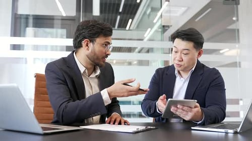 Two businessmen discussing business strategy at a meeting in modern office with digital tablet.