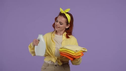 Mulher em roupas casuais em pé segurando uma pilha de setas dobradas e uma garrafa de amaciante com rosto sorridente