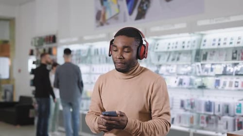 An African Man in an Eleutronics Store Chooses Wireless Headphones for Himself
