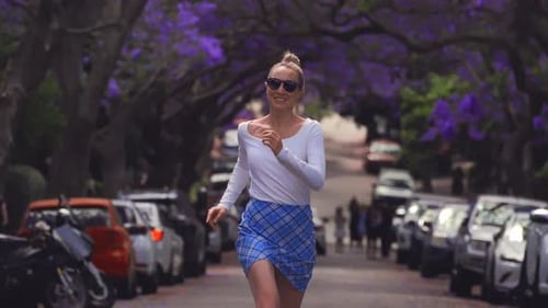 Energetic Female Runner Passing Parked Vehicles Beneath Vibrant Purple Blossoms On Spring Day