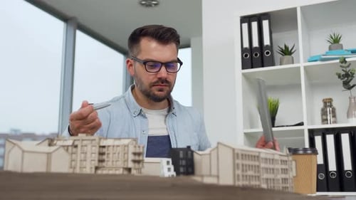 Man architect in glasses working with constructed model of new buildings in modern design office