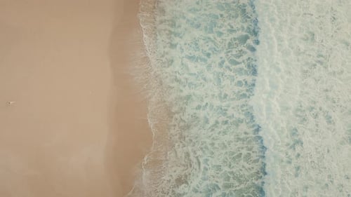 Blick von oben nach unten auf eine Frau, die auf den blauen Ozean zugeht und Fußabdrücke im Sand hinterlässt.