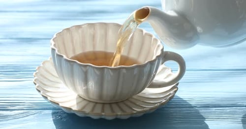 Heißen Tee aus der Teekanne am hellblauen Holztisch in eine Tasse gießen, Nahaufnahme
