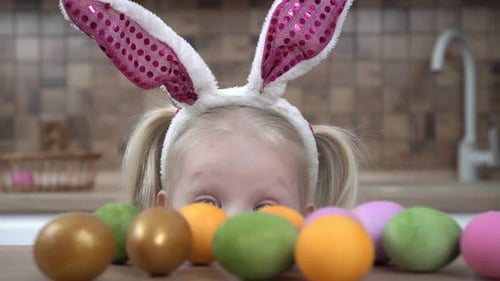Glückliches Kindermädchen mit Hasenohren freut sich über die Osterfeiertage Bunte Eier auf dem Küchentisch