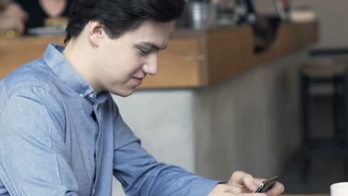 Young, Teenage Boy Playing Game on Smartphone Sitting in Cafe Adolescent