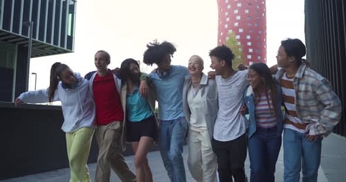 Multiethnic Group of Young Happy Friends Walking and Jumping Down the Street Holding Each Other