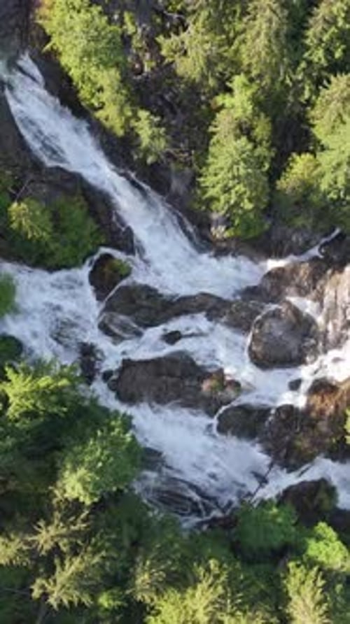 Majestic Waterfall Cascading Over Rocky Terrain Amidst Lush Green Trees in British Columbia, Canada.