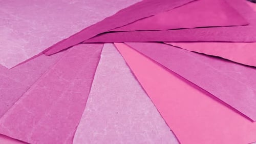 Rotating abstract background of textured pink, blush, berry and magenta handmade paper sheets.