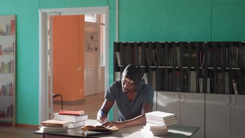 Mann studiert und schreibt Notizen in einer sonnenbeschienenen Bibliothek mit Bücherstapeln