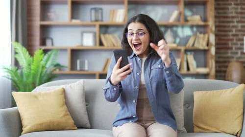 Excited Woman Reacting to Smartphone News on Couch