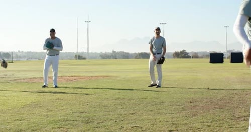 Diverse male teammates starting warm-up drill by catching and returning ball on field, with gloves