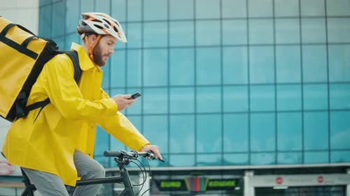 Handsome Delivery Person in Yellow Uniform Riding a Bike and Using Smartphone