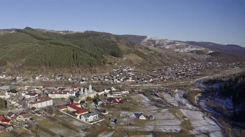 Drone view of Padure - city in the valley below a mountain range lined with pine trees and snow