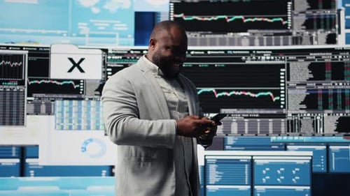 Man With Phone In Front of Data Displays