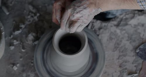 Vue en grand angle d'un magnifique vase tournant sur un volant et de mains masculines boueuses travaillant avec de l'argile
