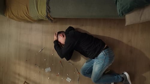 Top View of a Man Lying on the Living Room Floor Among Pills Syringes Close Up The Man is Suffering