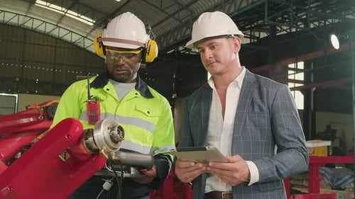 An engineer demonstrates robotic arm control to customer in industry factory.