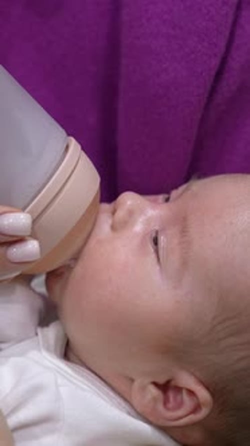 Baby Drinks Formula from Bottle Held by Adult