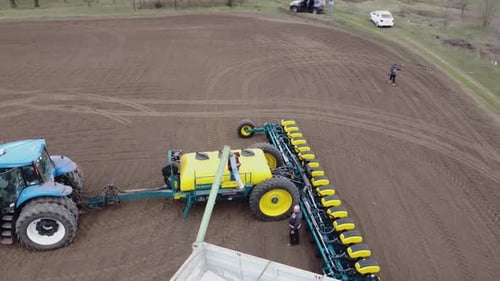 Blue tractor with yellow seeder working on the field in Ukraine OA