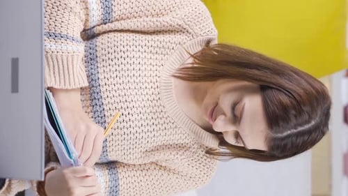 Vertical Video of Young female college student learning online using laptop, taking notes at home.