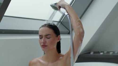 A Woman Stands Under a Showerhead Letting Water Run Over Her Hair and Body