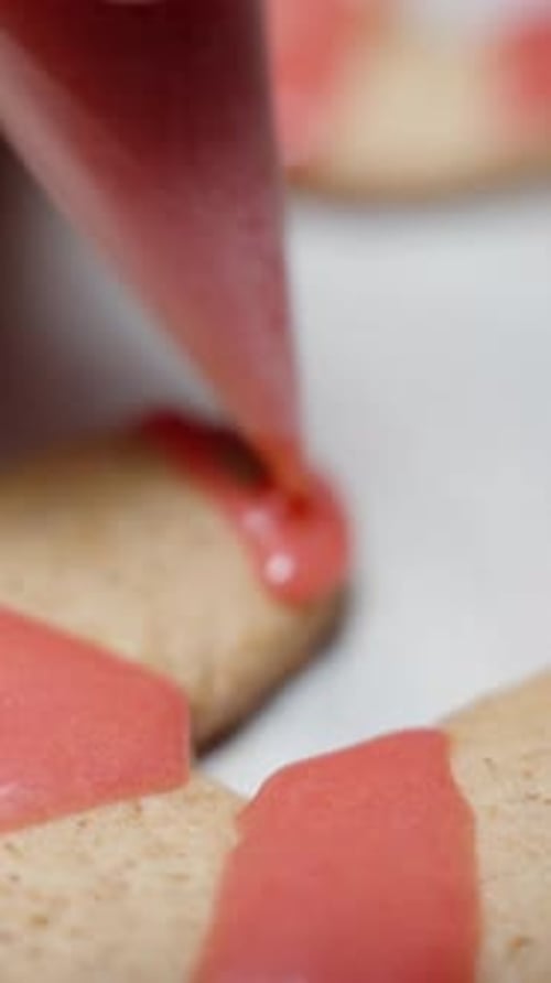Vertical video. Using a small pastry bag, the woman applies red icing to the gingerbread cookie