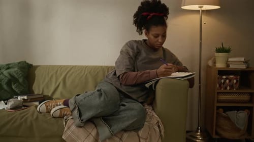 Motivated Black Teenage Girl Studying at Night on Couch at Home