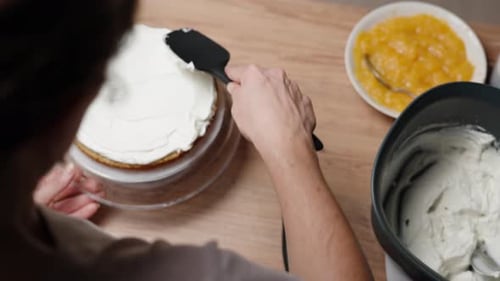 From behind the head, in slow motion, the view shows the woman preparing the cake, spreading cream