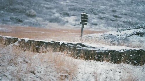 Sign-post with hiking trails. Light snow falls slowly and covers the landscape.